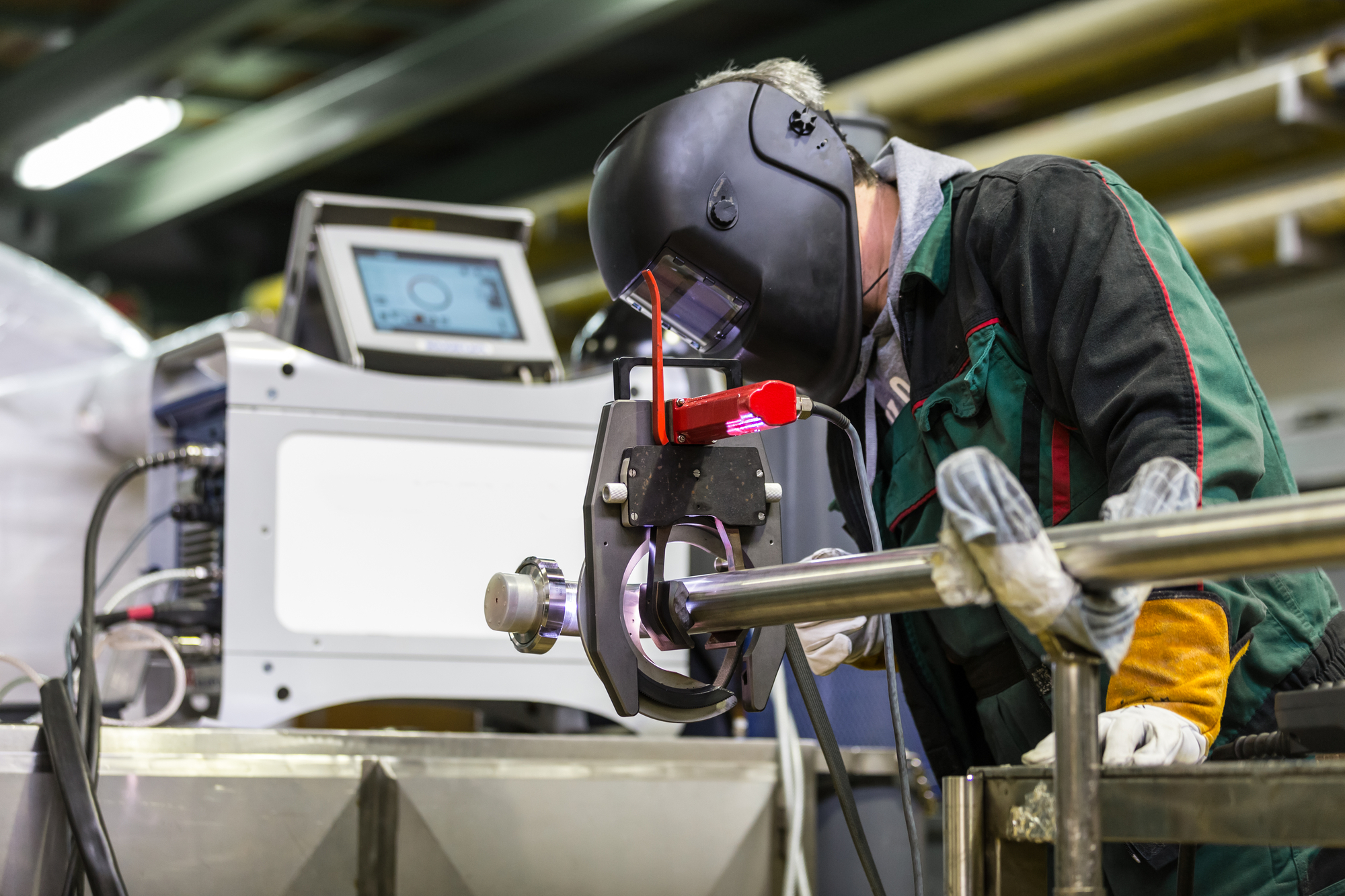 Industrial operator setting computer controlled process of orbital welding machine in inox pipes manufacturing workshop.