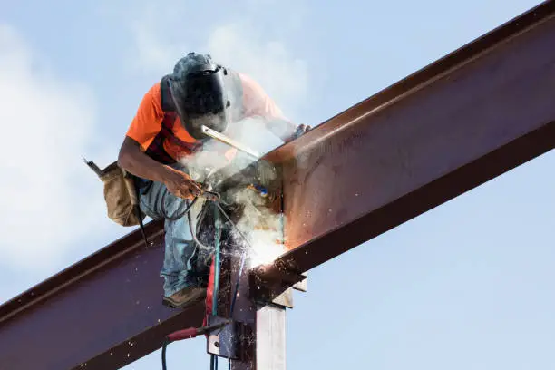 Image of a welder on a construction site welding steel beam with stick welder.