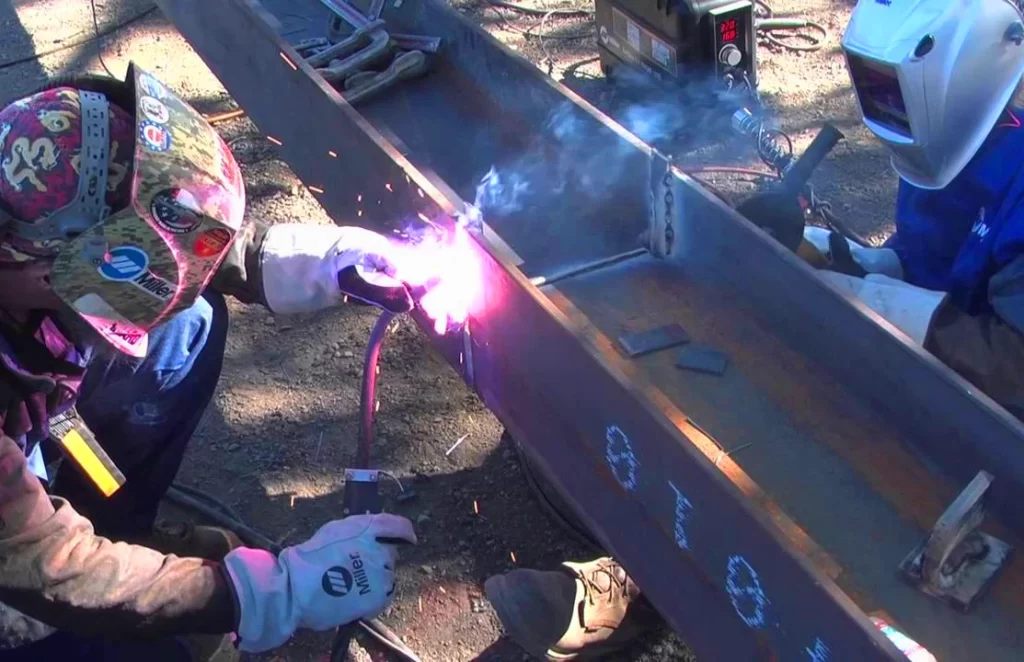 Image of a welder and his helper welding two steel beams together using dual shield welding process - Applications